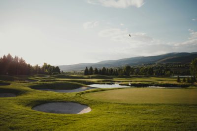 Hole with white flag and bunkers and a lake nearby with trees around and birds in the sky