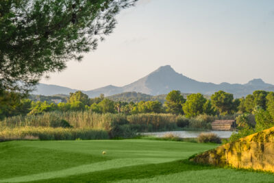 Tee box with trees and a pond around with mountains in the distance