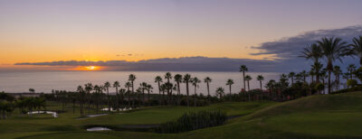 Fairway with bunkers, water hazards and trees around at Abama Golf Course with ocean view at sunset