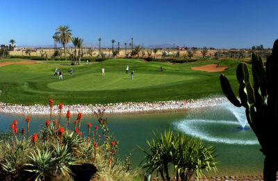 Lake with fountain before the green with three players and caddies at Amelkis Golf Course