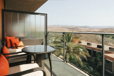 Balcony with seating with orange cushions and a round glass table, overlooking the surrounding area
