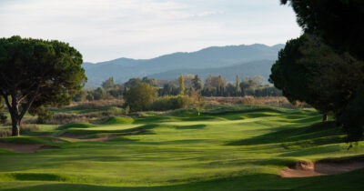 Bunkers on fairway with trees around leading to a hole with a yellow flag