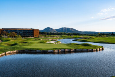 Lake on fairway with building, trees and mountains in distance at Hotel Terraverda