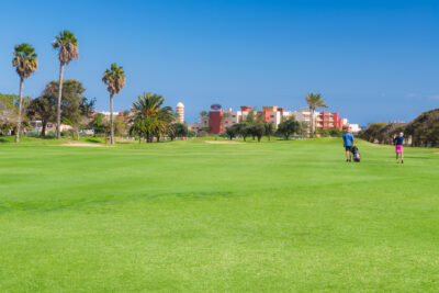 People playing golf at Fuerteventura Golf Club with trees around and building in background