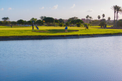 Lake near a hole with a yellow flag with bunkers around and people playing golf