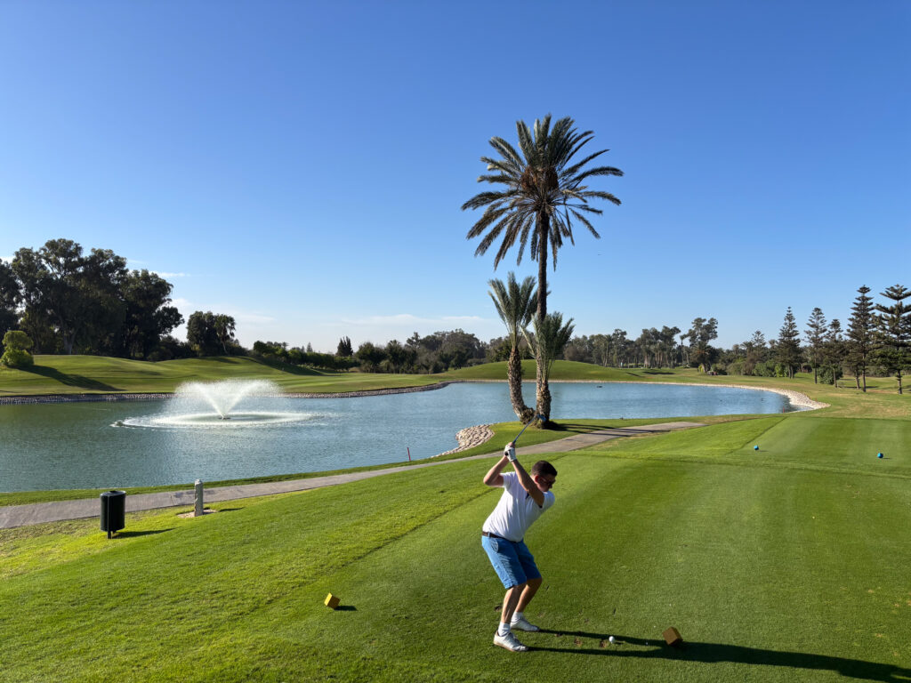 Tee box with man hitting tee shot with lake in background at Golf du Soleil