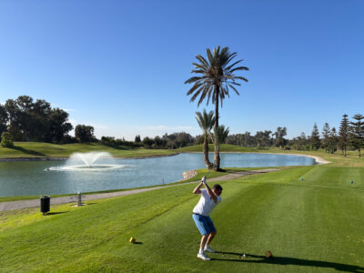 Tee box with man hitting tee shot with lake in background at Golf du Soleil