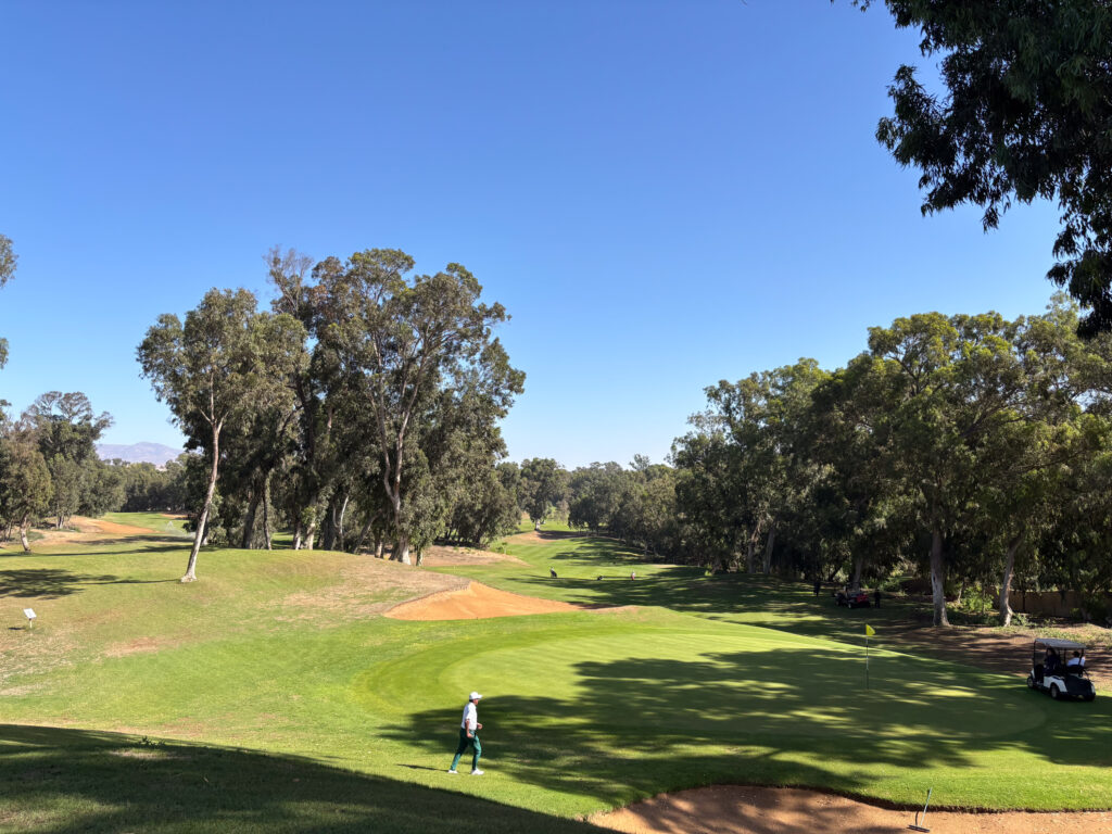 Green with man and wlaking over it and buggy off to the side of the green at Golf Les Dunes Course