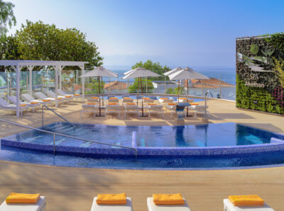 Outdoor pool with white sun loungers and yellow towels, with trees around