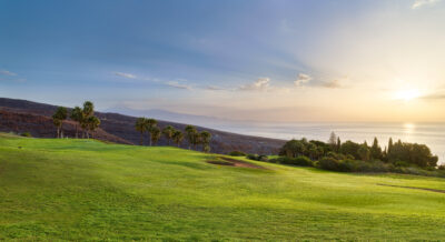Fairway with trees around and ocean in the distance on a sunny day