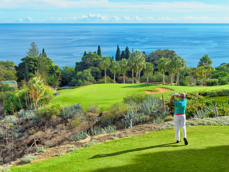 Person playing golf at Tecina Golf course with trees around and ocean in distance