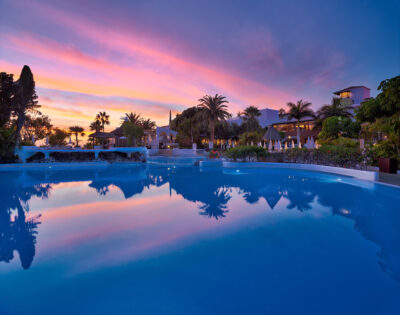 Outdoor pool with trees around and building in background at sunset