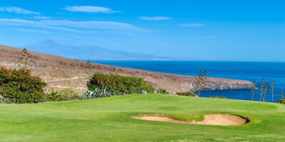 Hole with white flag and bunker with trees around and the ocean in the background