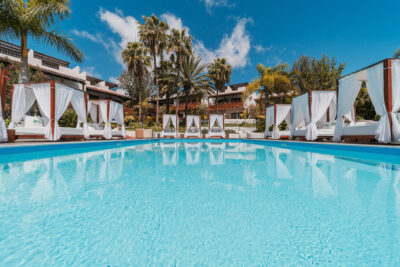 Outdoor pool with white curtained sun beds around and palm trees