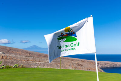 White flag with the Tecina Golf logo and ocean in the distance