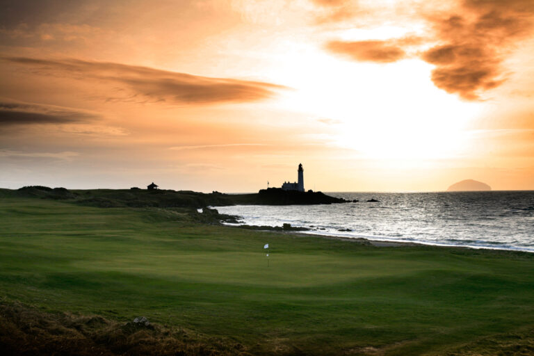 Hole with white flag at Trump Turnberry - Ailsa with ocean and lighthouse in background at sunset