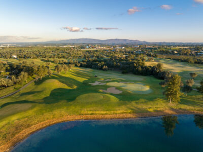 Aerial view of a green with bunkers around and a lake next to it, with trees lining the fairway
