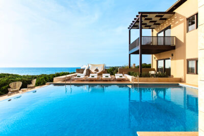 Outdoor pool with loungers at The Romanos Resort with beach in the distance
