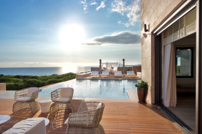 Outdoor pool with white chairs and sun loungers with the ocean in the distance