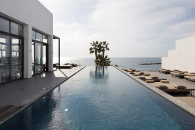 Outdoor pool with loungers and palm trees, overlooking the ocean