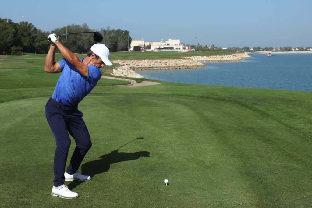 Person teeing off with view of the ocean and trees and buildings in the distance