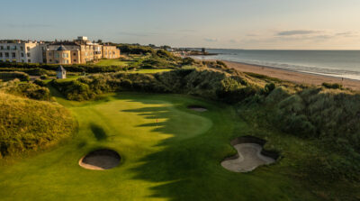 Hole with bunkers at Jameson Golf Links with view of the beach and buildings in background