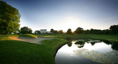 Bunker on fairway at Druids Glen Golf Course with lake next to it and trees in background