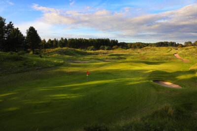 Hole with red flag at Formby Ladies Golf Club with trees around