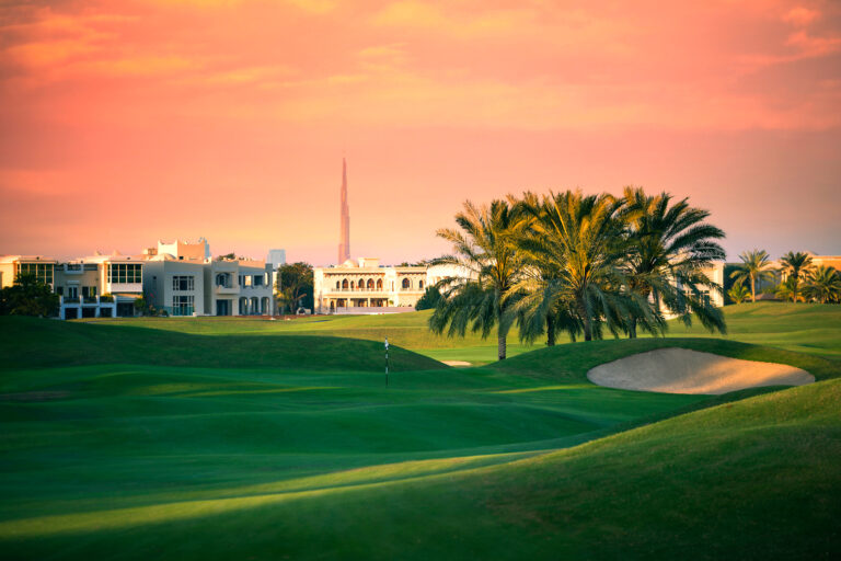 Hole with bunker at Montgomerie Golf Club Dubai with trees around and buildings in distance