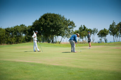 People putting on a green at Lighthouse Golf Course with trees in the background