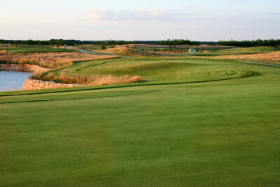 Fairway with tall grass and a lake nearby at Lighthouse Golf Course