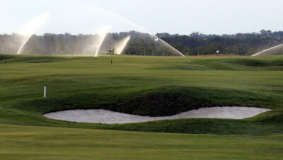 Bunker on fairway with sprinklers on in the background and trees in the distance
