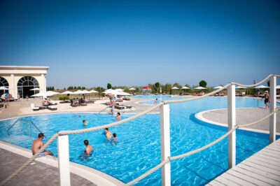 Outdoor pool with people swimming and sun loungers in the background