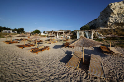 Sun loungers on the beach with straw umbrellas and a bar in the background