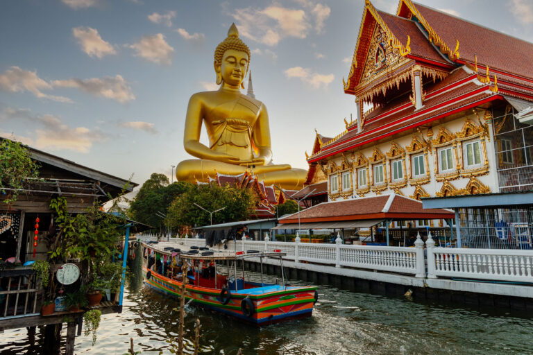 front of a buddha temple in Thailand with a river and boat on the side